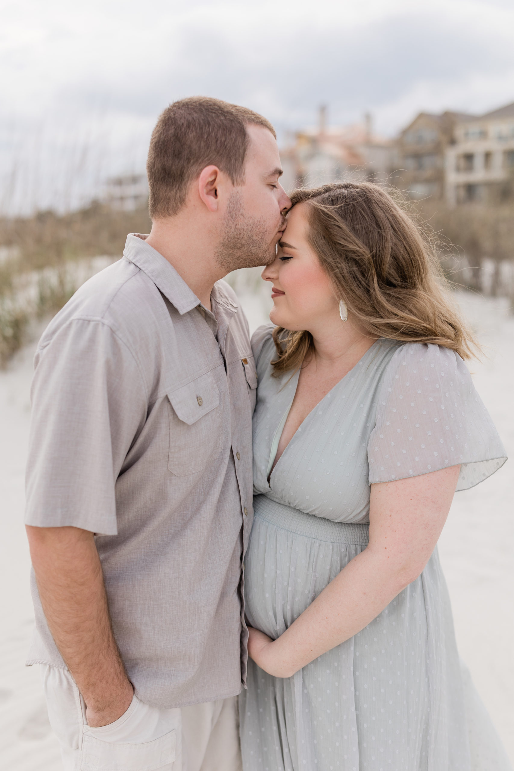 a pregnant couple kissing on the beach.