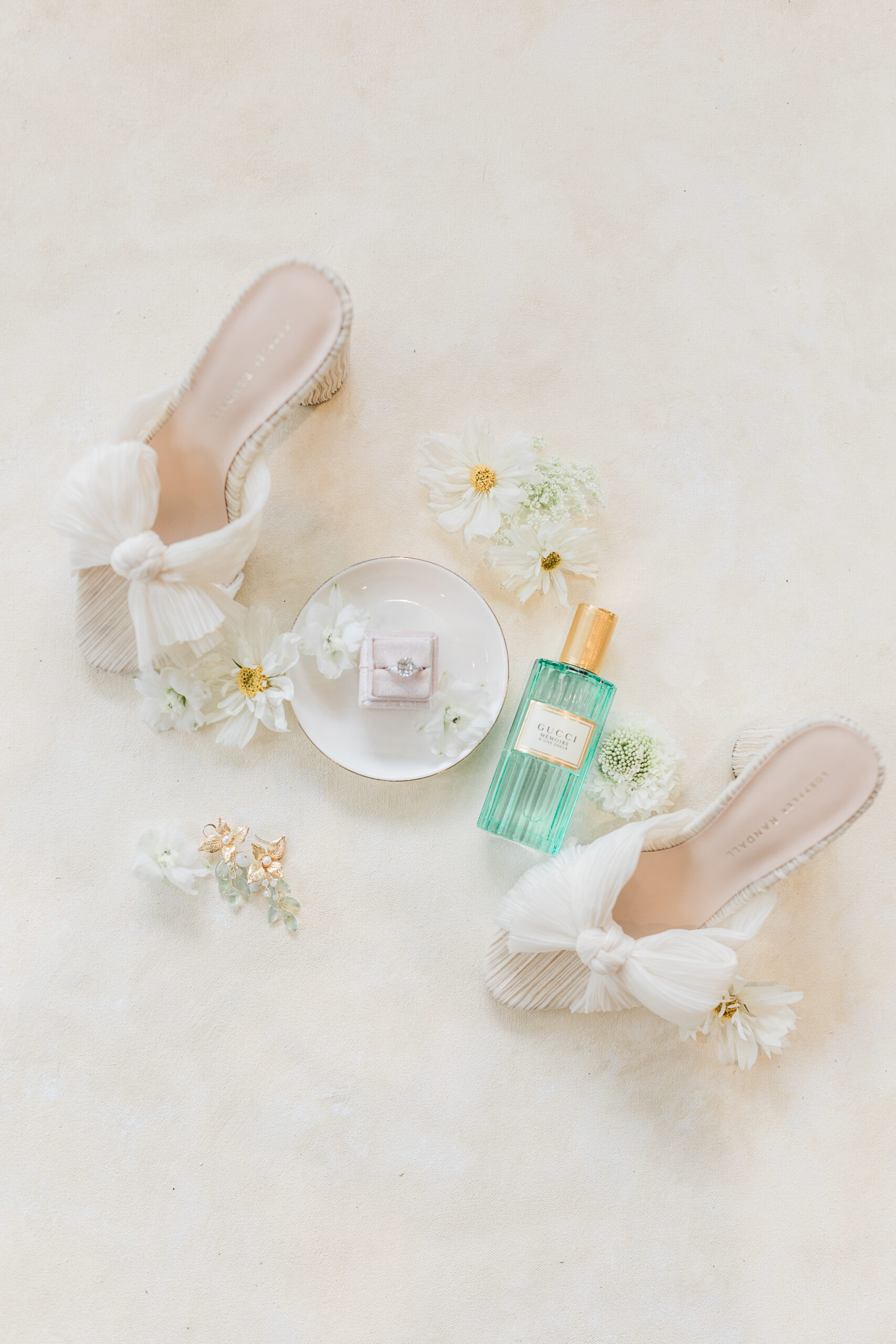 A pair of white shoes and a bottle of perfume on a white surface.